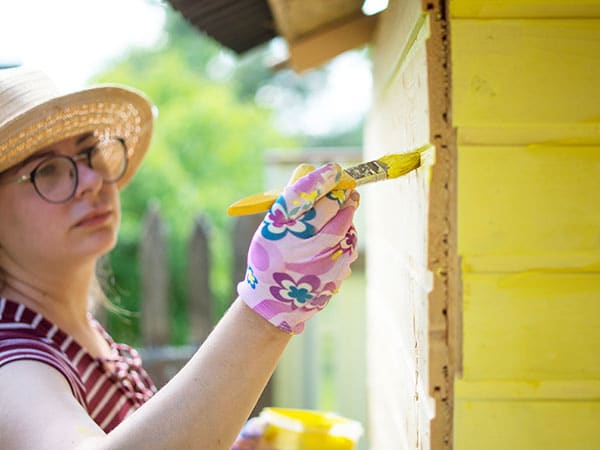 Une employée d'ARIL Services qui peint un abri de jardin